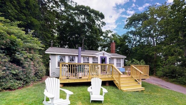 A small house with a deck, two Adirondack chairs, and a staircase leading to a porch. - Dog-friendly Fisher Hill Home With Patio and Wood Stove - Walk to the Harbor (Boothbay Harbor)