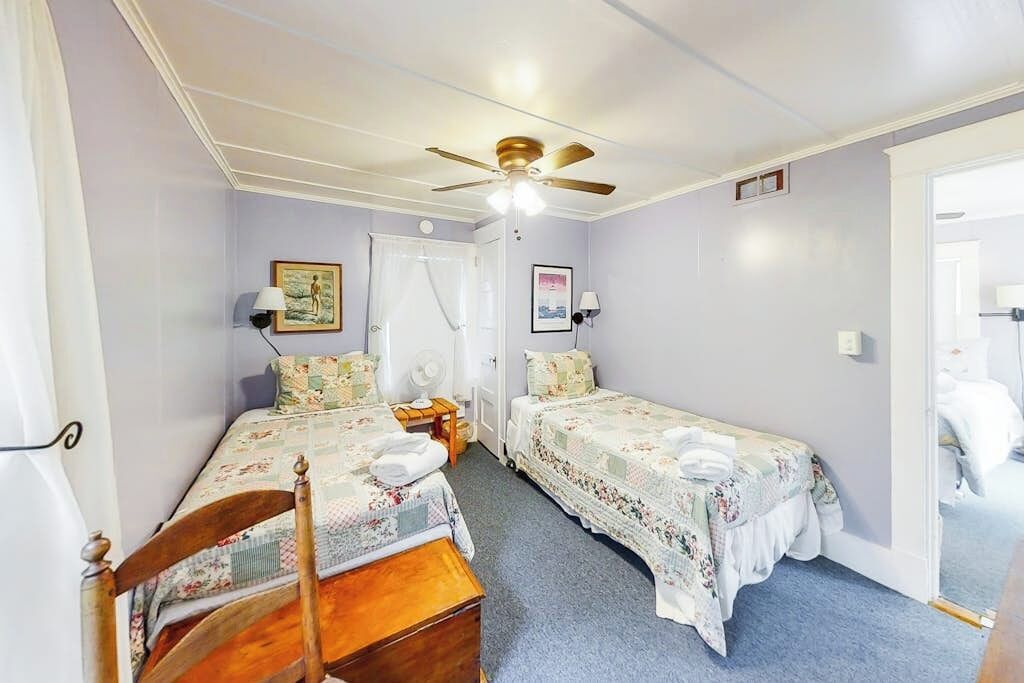 Une chambre avec deux lits simples, un ventilateur de plafond, une porte et une petite table.