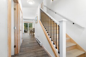 A staircase with wooden steps and black balusters, leading to a landing with a view of outdoor greenery.