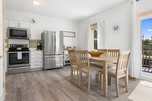 A modern kitchen with stainless steel appliances, a dining area with wooden chairs, and a view of the outdoors.