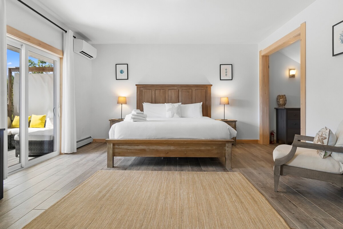 Una camera da letto con un letto in legno, due lampade ai comodini, vista su una zona esterna e un piccolo angolo salotto con una sedia e un tavolo.