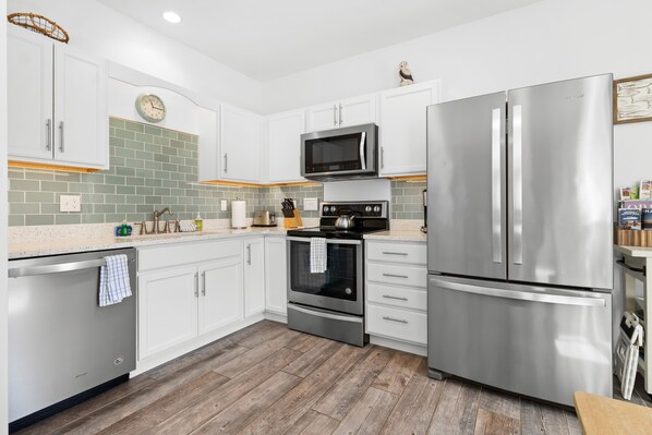 A modern kitchen with white cabinetry, stainless steel appliances, a microwave, oven, and a refrigerator.