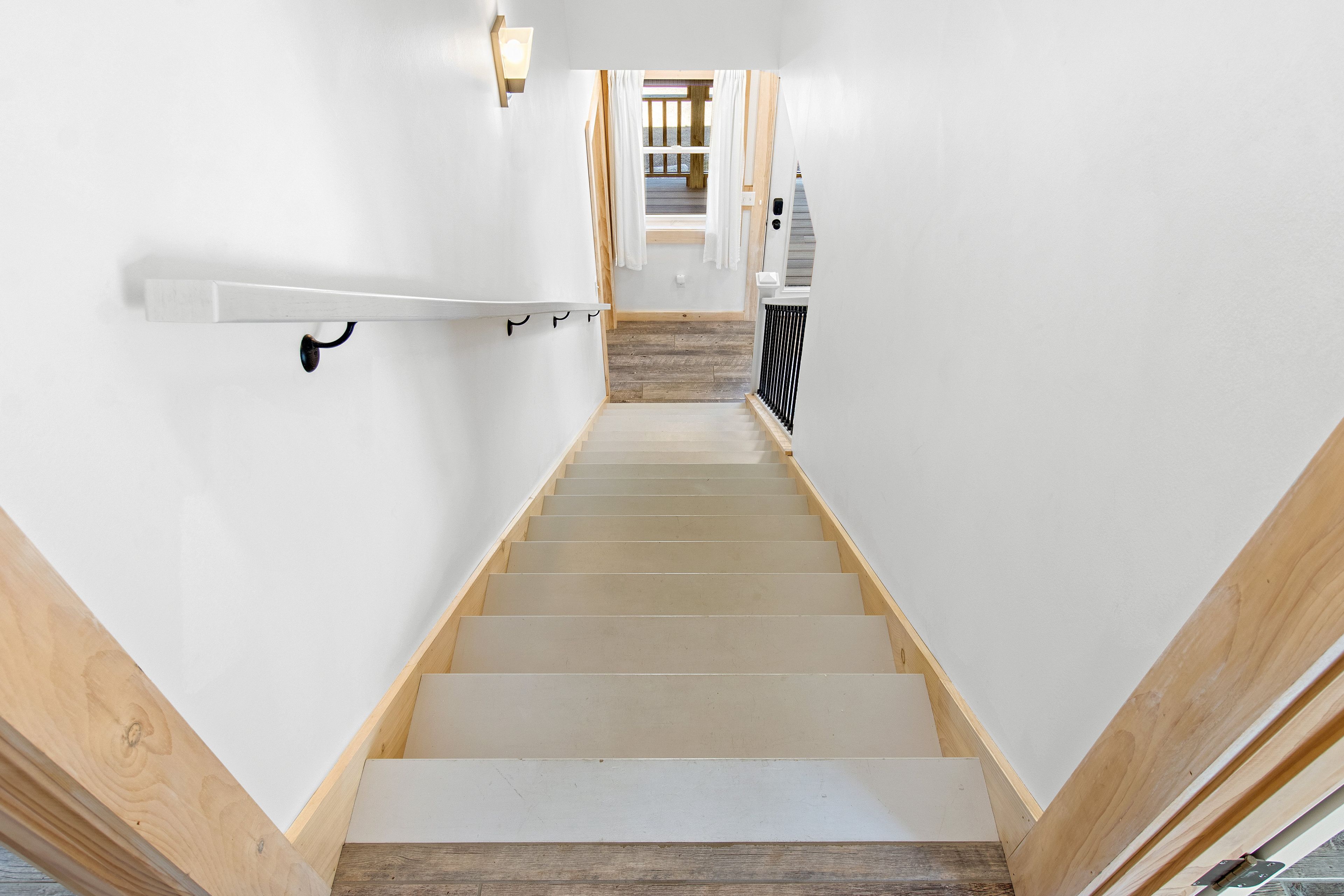 Un escalier avec des marches en bois et des murs blancs, menant à une pièce dotée d’un plancher en bois et d’une fenêtre.