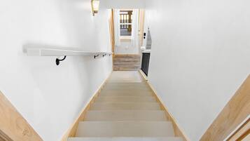 Un escalier avec des marches en bois et des murs blancs, menant à une pièce dotée d’un plancher en bois et d’une fenêtre.