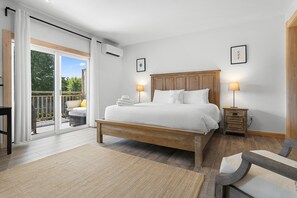 A bedroom with a wooden bed, two bedside tables, a large window with a view of greenery, and a balcony. - Ocean Breeze (Owls Head)