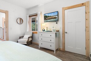 A bedroom with a bed, a chair, a dresser, a television, and a door.