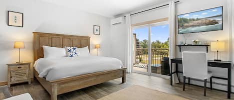 Un dormitorio con cama, mesitas de noche, escritorio, una silla y vistas al exterior a través de una puerta corredera.