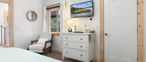 Een slaapkamer met een bed, een stoel, een dressoir, een televisie en een deur.