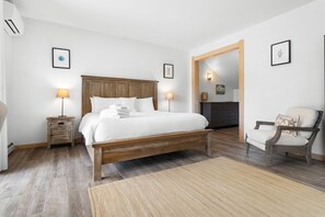 A bedroom with a wooden bed, bedside lamps, a chair, and a rug. - Ocean Breeze (Owls Head)