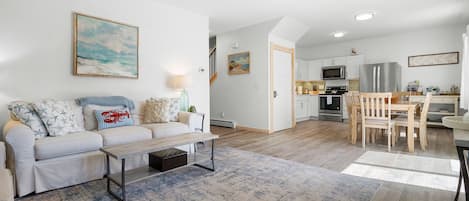 A modern living room with a sofa, coffee table, and a dining area with a wooden table and chairs.