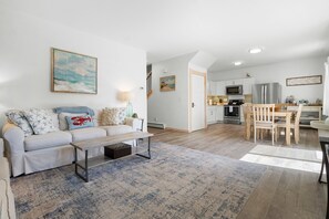A modern living room with a sofa, coffee table, and a dining area with a wooden table and chairs. - Ocean Breeze (Owls Head)