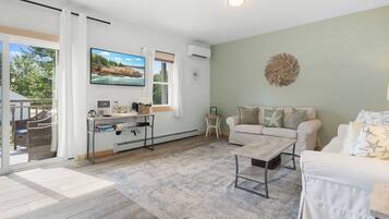 A spacious living area with a large window, a flat-screen TV, a sofa, and a coffee table.