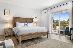 A bedroom with a wooden bed, two bedside tables with lamps, a large window with a view of the outdoors, and two framed pictures on the wall. - Ocean Breeze (Owls Head)