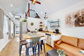 A modern kitchen with a central island, wooden flooring, and a cozy seating area with a leather sofa. - Brand-new Dog-friendly Home Near Hancock Pond With Firepit, Grill, Streaming, AC (Bucksport)