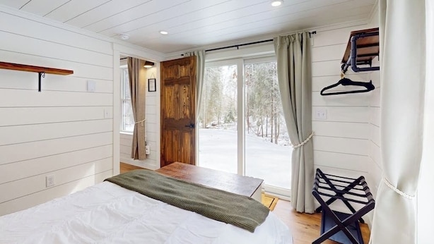 Ein Schlafzimmer mit Bett, Holztür und Blick auf eine verschneite Landschaft.