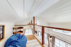 A high-ceilinged room with exposed wooden beams, a fireplace, and a view of the outdoors. - Brand-new Dog-friendly Home Near Hancock Pond With Firepit, Grill, Streaming, AC (Bucksport)