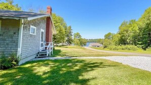 A single-story house with a front porch, a chimney, and a gravel driveway. - Classic Home Overlooking the St. George River With Deck & Great Views (Tenants Harbor)