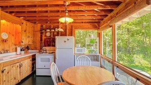 A wooden cabin interior with a kitchen, dining area, and large windows. - Classic Home Overlooking the St. George River With Deck & Great Views (Tenants Harbor)