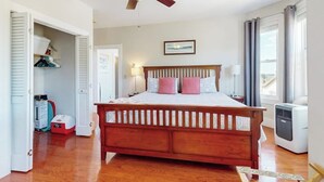 A bedroom with a wooden bed, a ceiling fan, a bedside table, a lamp, and a window with curtains. - Admiral's Quarters (Boothbay Harbor)