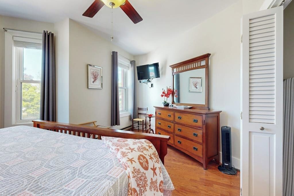 Een slaapkamer met een bed, een dressoir, een televisie en een plafondventilator.