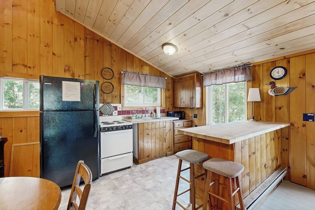 A wooden cabin kitchen with a refrigerator, stove, and bar stools.