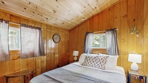 A wooden-paneled bedroom with a bed, two bedside tables, and curtains. - Quiet Lakefront Cottage With a Firepit, Private Beach, & two Kayaks (Ellsworth)