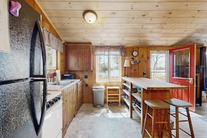 A compact kitchen with wooden cabinets, a refrigerator, a sink, and a window. - Quiet Lakefront Cottage With a Firepit, Private Beach, & two Kayaks (Ellsworth)
