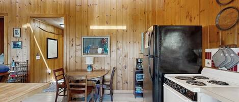 A kitchen with wooden walls, a dining table with chairs, a refrigerator, and a stove.