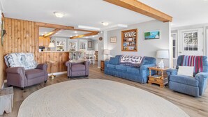 A spacious living area with a large round rug, two sofas, a coffee table, and wooden beams on the ceiling. - Cobbossee Hideaway, Lakefront Property With Dock for Swimming, Fishing, and Sunrises (Winthrop)