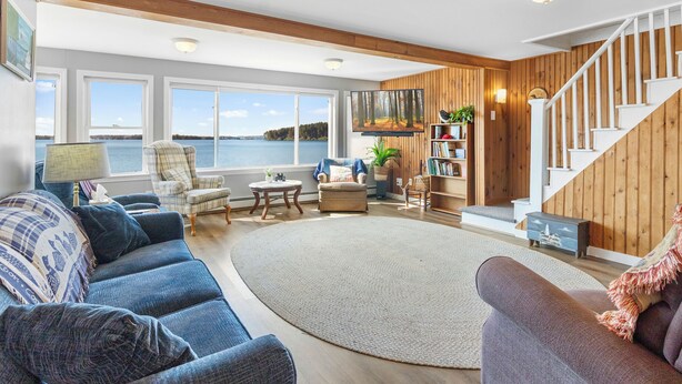 A spacious living room with a large window overlooking a body of water, a staircase, and a cozy seating area. - Cobbossee Hideaway, Lakefront Property With Dock for Swimming, Fishing, and Sunrises (Winthrop)