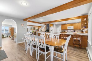 A spacious kitchen with wooden beams, white cabinetry, and a dining area with white chairs. - Cobbossee Hideaway, Lakefront Property With Dock for Swimming, Fishing, and Sunrises (Winthrop)