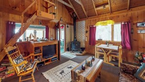 Ein Holzblockbau-Innenraum mit Kamin, Holzmöbeln, einem Fernseher und einer Treppe.