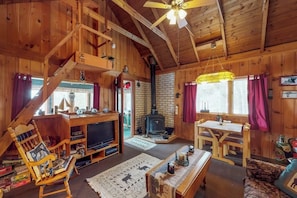 Ein Holzblockbau-Innenraum mit Kamin, Holzmöbeln, einem Fernseher und einer Treppe.