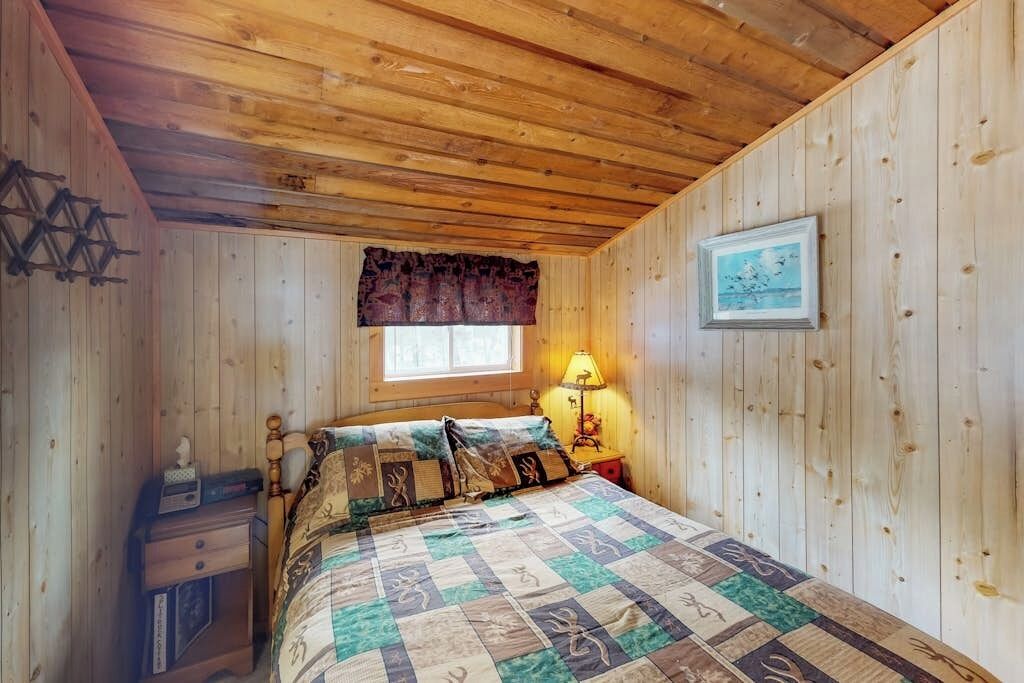 A wooden-paneled room with a bed, a nightstand, a lamp, and a framed picture on the wall.