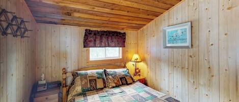 A wooden-paneled room with a bed, a nightstand, a lamp, and a framed picture on the wall.