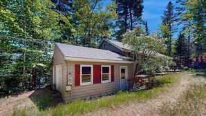 A small, single-story house with a sloped roof, a front door, and a small porch. - Lady Slipper Cottage: Charming Lakefront Retreat With Canoes, Kayaks, and Modern Comforts (Mount Desert)