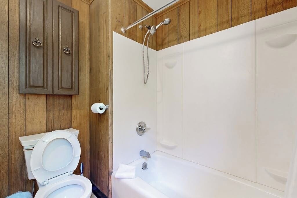 A bathroom with a toilet, a shower, and wooden paneling.