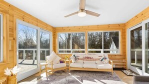Un intérieur de chalet chaleureux avec un plancher en bois, un ventilateur de plafond, un canapé et de grandes fenêtres.