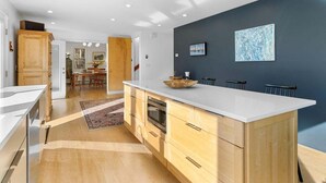 Une cuisine moderne dotée d’un grand îlot central, de meubles en bois et d’un mur d’accent de couleur foncée.