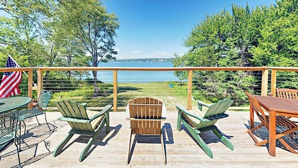 A deck with outdoor furniture, a grill, and a view of a lake. - Renovated Waterfront Cottage With Expansive Deck, Multiple Fireplaces, & Grill (Ellsworth)