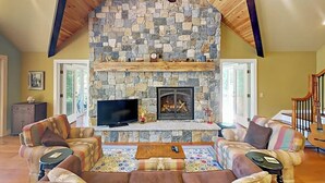 A cozy living room with a stone fireplace, comfortable seating, and a television. - Renovated Waterfront Cottage With Expansive Deck, Multiple Fireplaces, & Grill (Ellsworth)