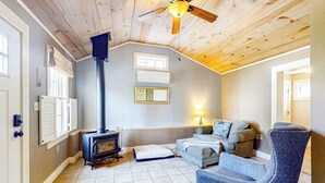 Ein gemütliches Wohnzimmer mit Kamin, einer Couch, einem Sessel und einem Deckenventilator.