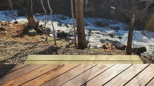 Eine Holzterrasse mit Blick auf einen Fluss, Bäume und Felsen.