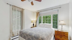 Ein Schlafzimmer mit einem Bett, zwei Nachttischen, einem Deckenventilator und einem Fenster mit Vorhängen.