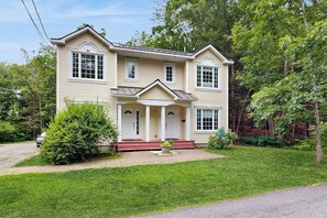 A two-story house with a front porch, a driveway, and a well-maintained lawn. - Convenient Home With Deck, Grill, & Washer/dryer - Walk Into Town & Acadia (Bar Harbor)