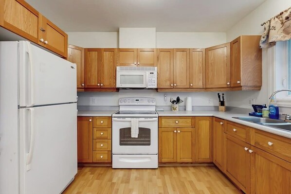 Una cocina con armarios de madera, un refrigerador blanco, un microondas, un horno y un fregadero.