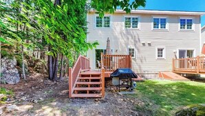 Ein zweistöckiges Haus mit einer Terrasse, einem überdachten Grillbereich und einer Steinmauer.