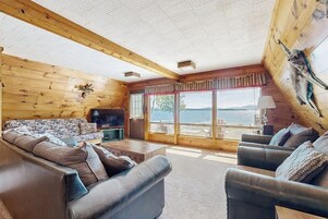 Interior de una cabaña de troncos con un sofá, una televisión y vistas al exterior.