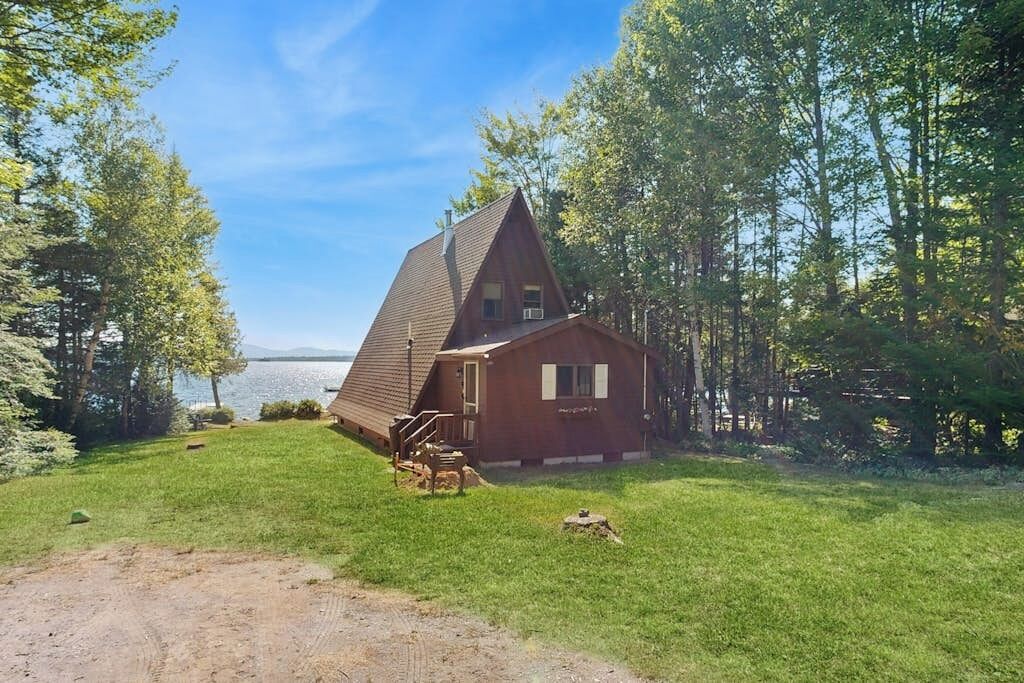 A cabin with a sloped roof, a deck, and a view of a lake.