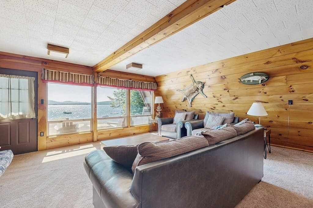 A cabin interior with a large window, wooden walls, a sofa, and a lamp.